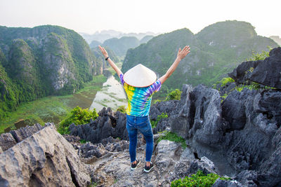 Rear view of man with arms raised standing on mountain