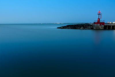 Lighthouse by sea against clear blue sky