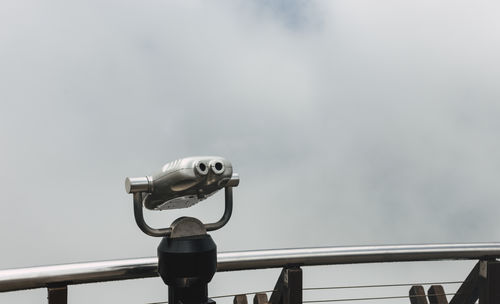 Low angle view of coin-operated binoculars against cloudy sky