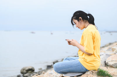 Young man using mobile phone while sitting on beach