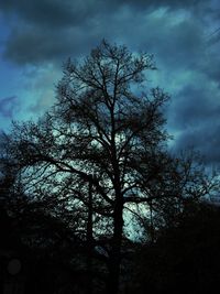 Low angle view of bare trees against cloudy sky