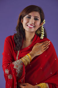 Portrait of beautiful indian woman in red sari against purple background