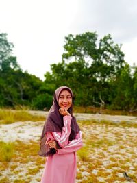 Portrait of a smiling young woman standing against trees