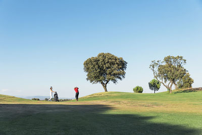 People walking on golf course against clear sky