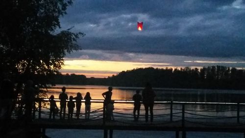 Silhouette people on shore against sky during sunset