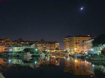 Illuminated buildings by lake against sky at night