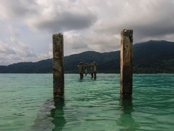 Wooden posts in sea against sky