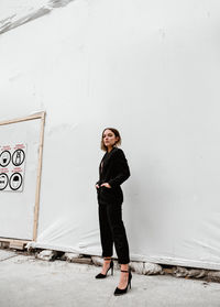 Full length portrait of young woman standing against wall