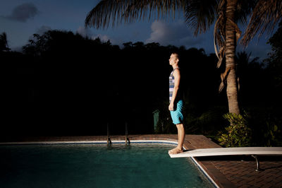 Side view of man standing on diving platform over swimming pool