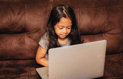 Cute girl using laptop while sitting on sofa at home