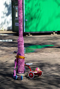 Bicycle and push scooter by crocheted pole on footpath