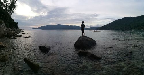 Man standing on rock by sea against sky