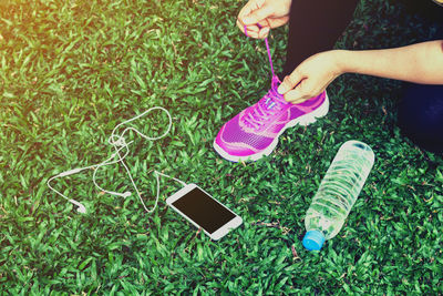 Low section of woman tying shoelace against grass at field