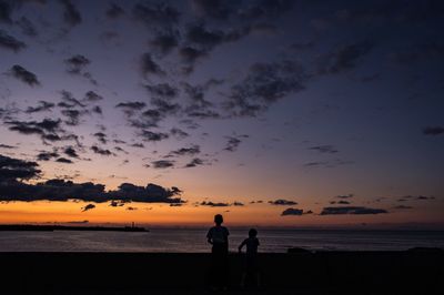 Silhouette friends standing on beach against sky during sunset