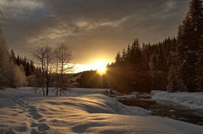 Snow covered landscape against sky during sunset