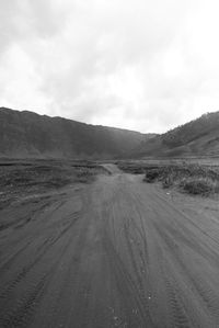 Dirt road passing through land against sky