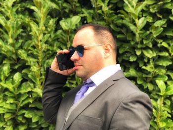 Businessman in sunglasses talking on mobile phone against plants