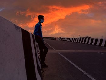 Man standing on road against sky during sunset