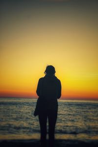 Rear view of silhouette young woman standing on beach during sunset