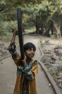 Boy looking away while carrying tire on footpath at park