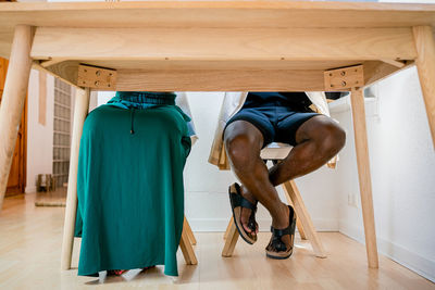 Unrecognizable man and woman in casual clothing having break at small wooden table in bright apartment