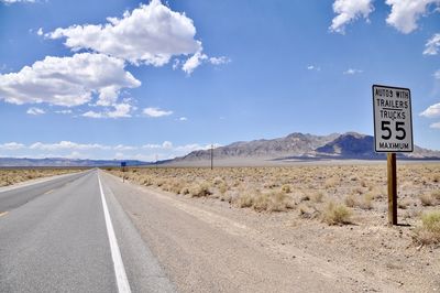 Information sign on road by landscape against sky