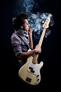 Portrait of a man with a guitar and a cigarette on a dark background and a light blue shirt