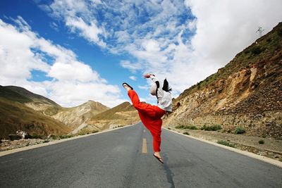 Woman leaping on road against mountains