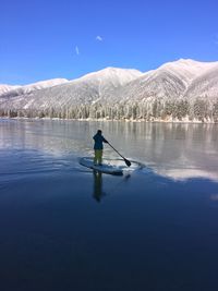 Rear view of man paddleboarding in lake against blue sky