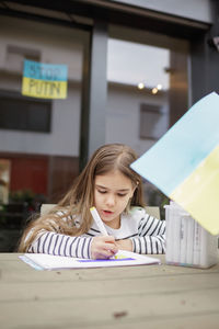 Small girl draws ukrainian flag in safe place abroad in europe where she fled from russian invasion