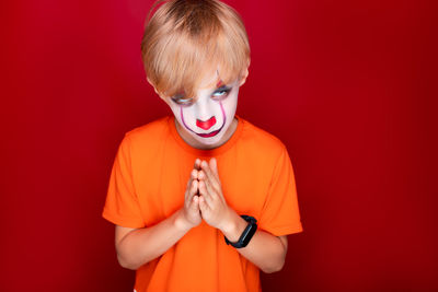 Portrait of boy holding red face against orange background