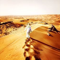 People walking on sand dune in desert against sky