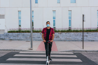 Unrecognizable trendy male in face mask riding electric scooter on city road during covid 19 pandemic