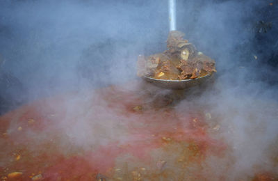 Cooking traditional meat curry in a large pan on a wood fire at indonesian street food market