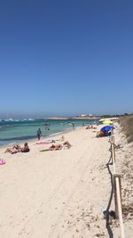 People on beach against clear blue sky