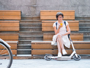 Full length of woman using phone sitting on bench