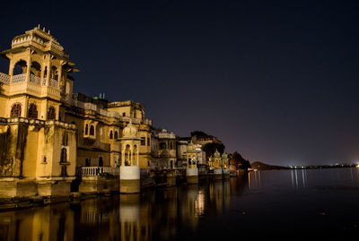 Illuminated heritage buildings by lake against sky at night