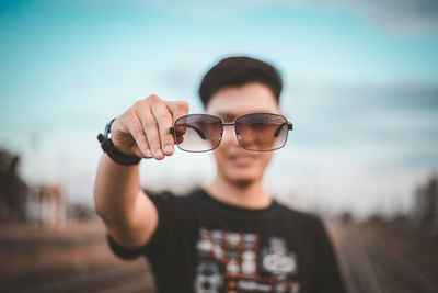 Portrait of young man wearing sunglasses standing against sky