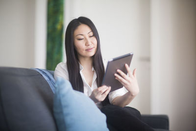 Young woman at home in a living room lying on a couch with tablet