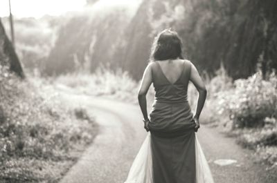 Rear view of woman walking on road in forest