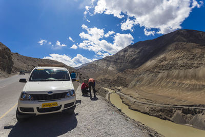 People on road by mountains against sky