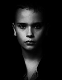 Close-up portrait of serious boy against black background