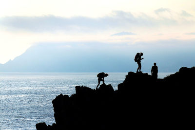 Silhouette people standing on rock by sea against sky