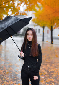 Young woman standing by tree during autumn
