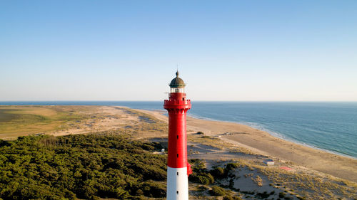 Lighthouse by sea against clear sky