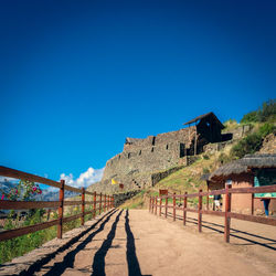 Footpath by buildings against clear blue sky