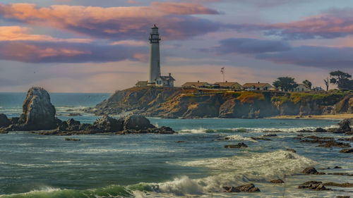 Lighthouse by sea against sky during sunset