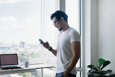 Man using mobile phone while standing by window