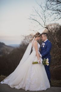 Bride holding flower bouquet with groom embracing against sky