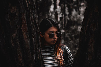 Portrait of beautiful young woman standing by tree trunk